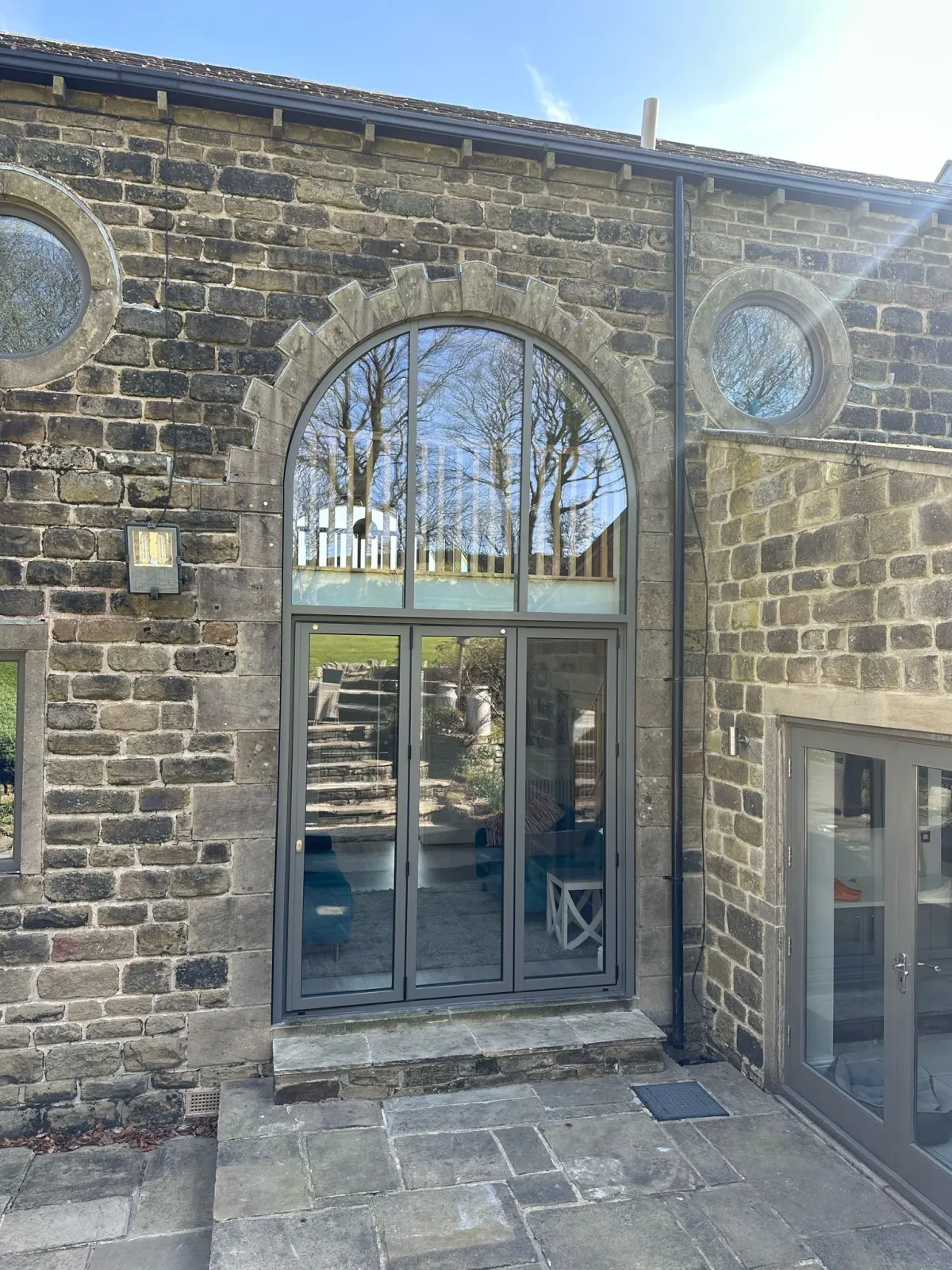 Aluminium bi-fold doors beneath arched glazing in a stone elevation